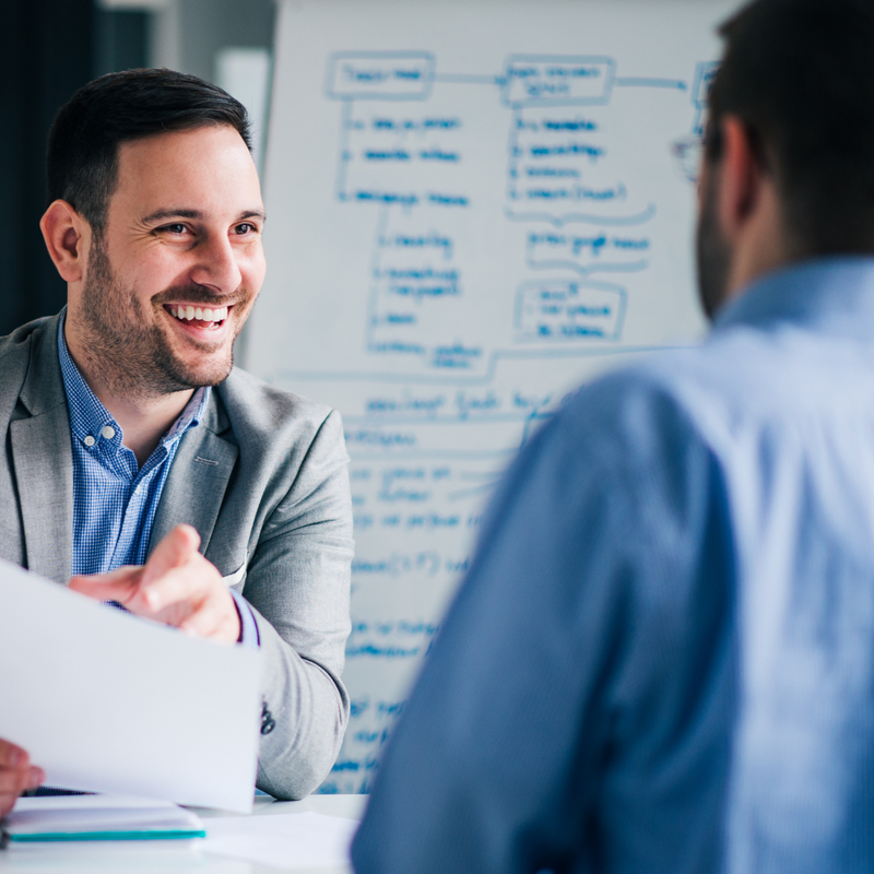 Bearded man talking to a colleague while pointing to a sheet of paper