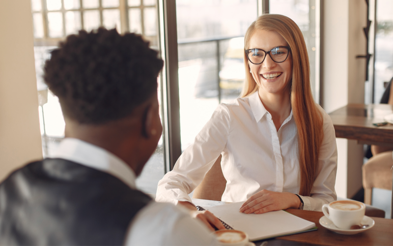 Professional woman with glasses at at a desk talking to a man with his back to the camera