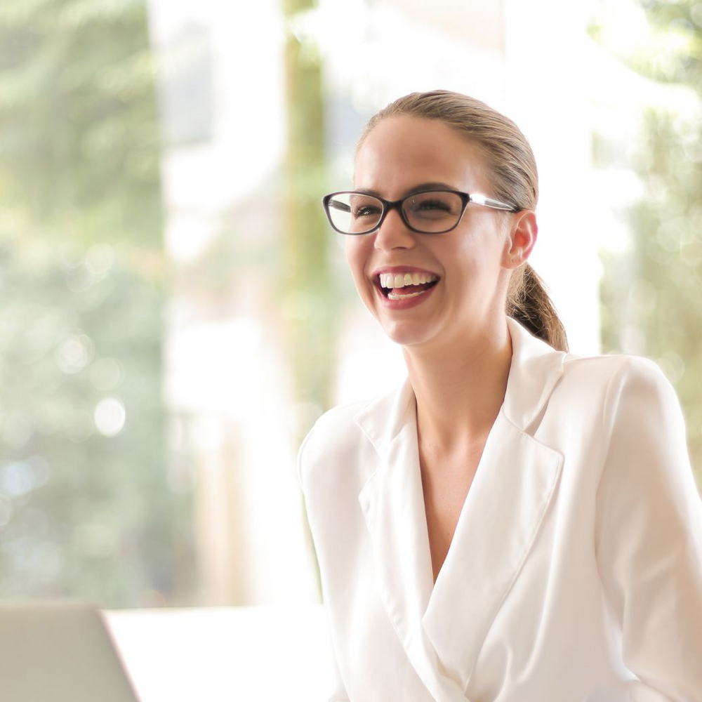 Professional businesswoman wearing white blouse sitting at a desk, with an open laptop and smiling