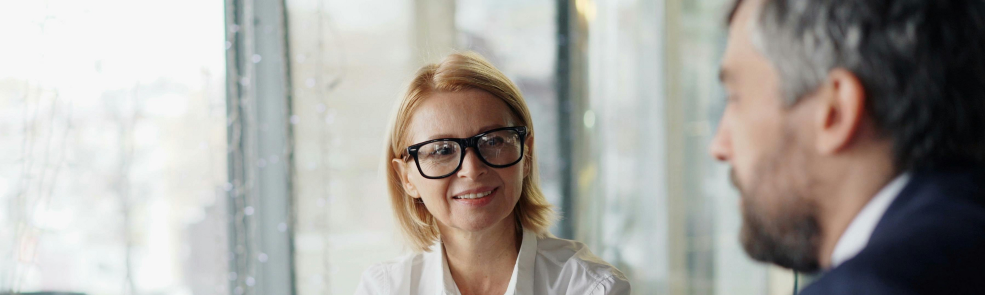 Professional businesswoman wearing glasses looking at a man in the foreground