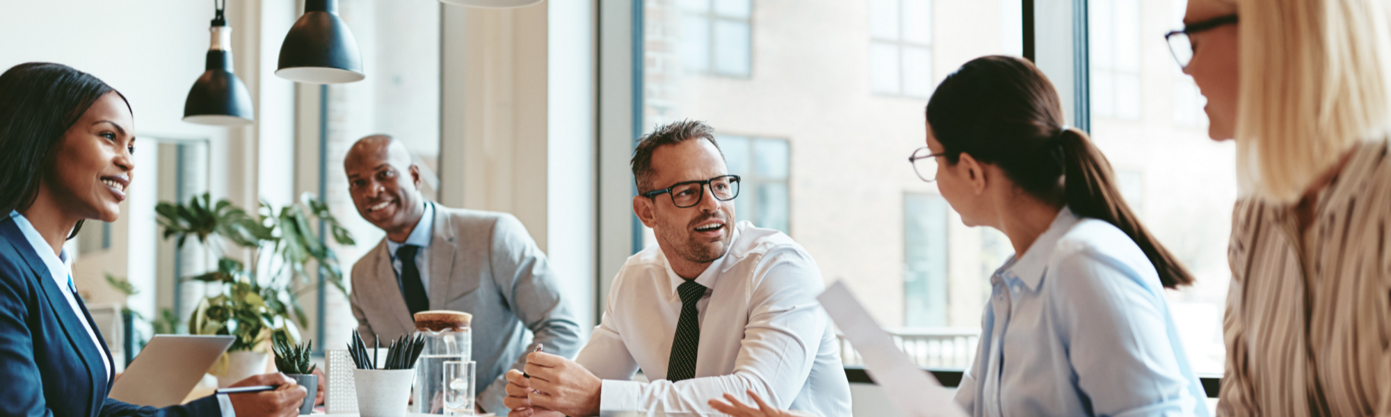 Man with glasses on at a table, talking with colleagues