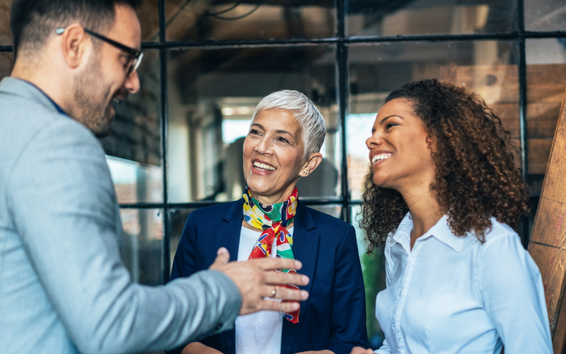 Two women and a man dressed in smart work clothes engaged in conversation