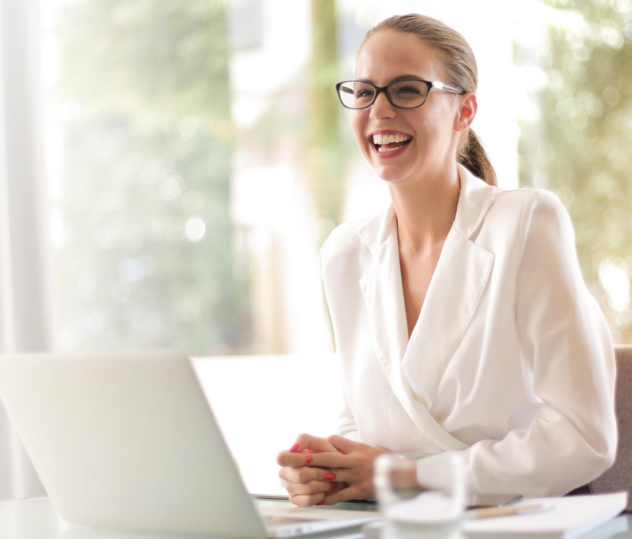 Professional businesswoman wearing white blouse sitting at a desk, with an open laptop and smiling