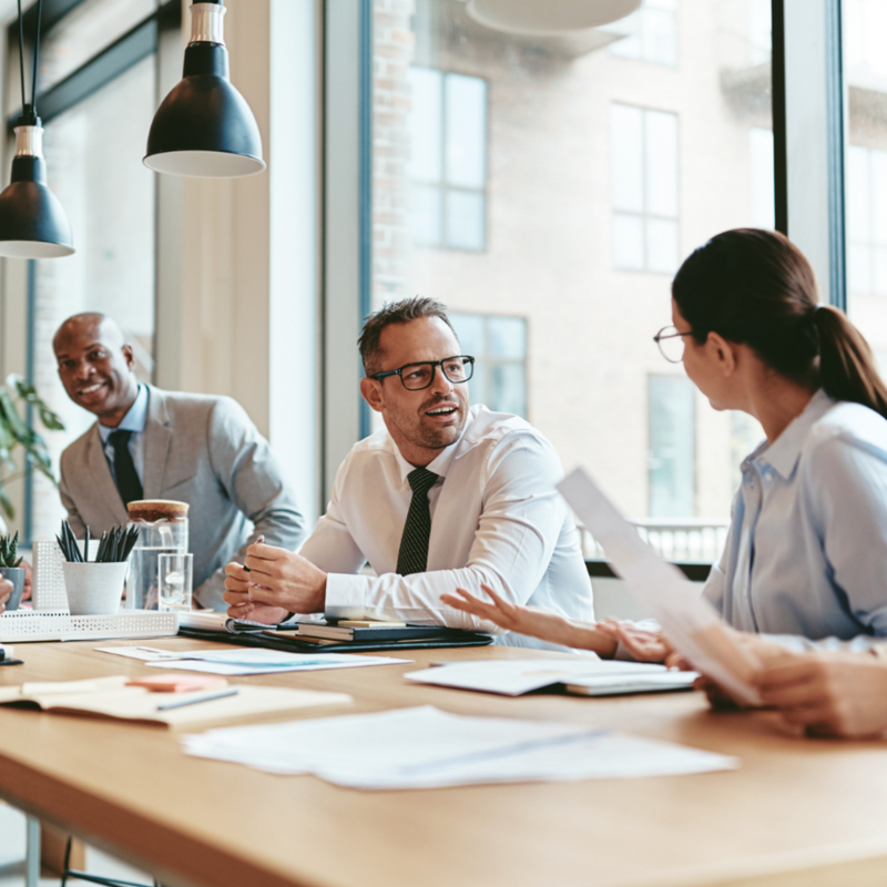 Businessman sitting in a business meeting talking to a woman on his left