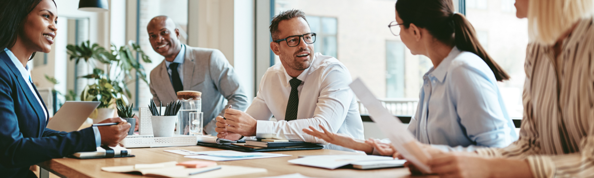 Man with glasses on at a table, talking with colleagues