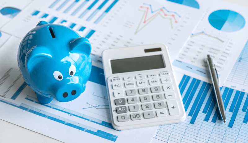 Blue piggy bank, calculator and a pen on top of financial documents