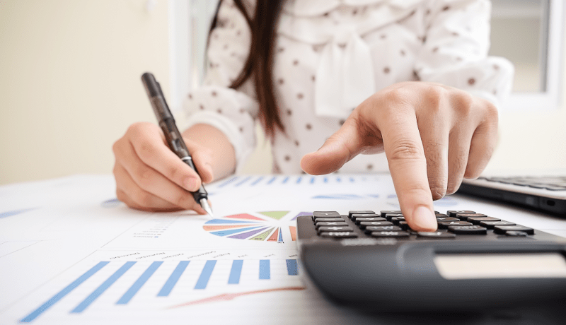 Woman holding a pen while pressing buttons on a calculator
