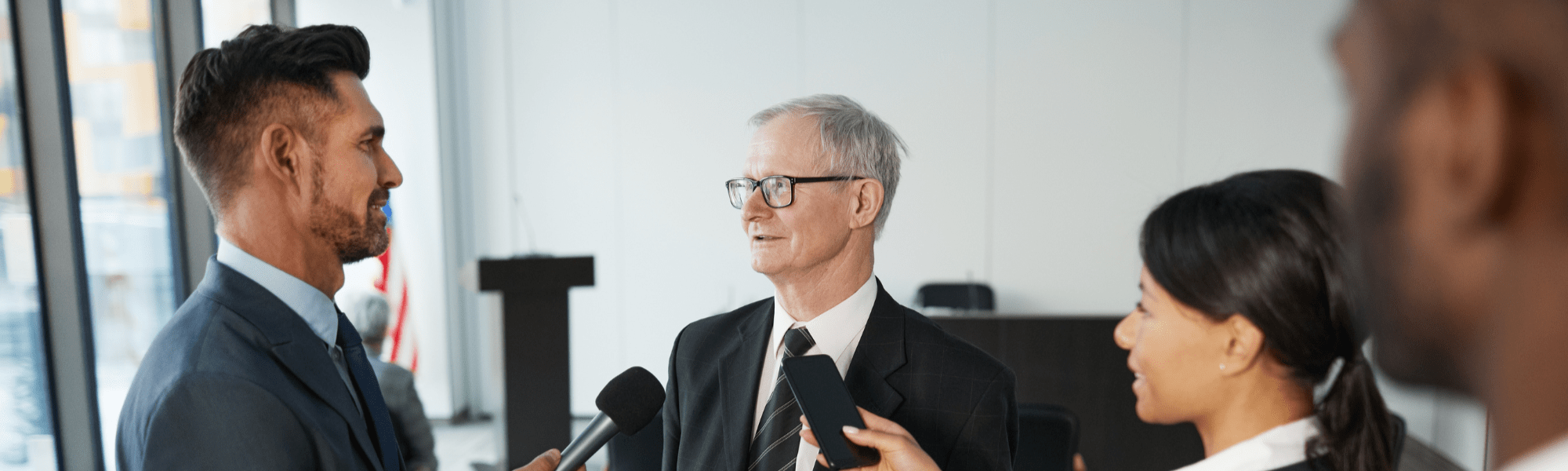 Businessman being interviewed while flanked by reporters holding microphones and recording devices
